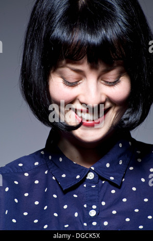 Young woman in blue spotted blouse looking down, smiling Stock Photo