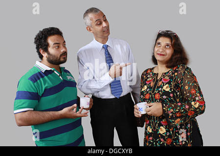 Colleagues discussing in a coffee break, two men, one woman, two people having coffee cups in hand Stock Photo
