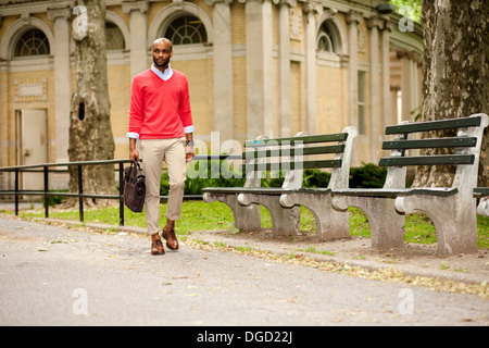 Young man carrying briefcase through park Stock Photo