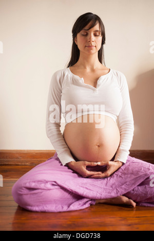 Pregnant woman meditating whilst sitting on floor Stock Photo