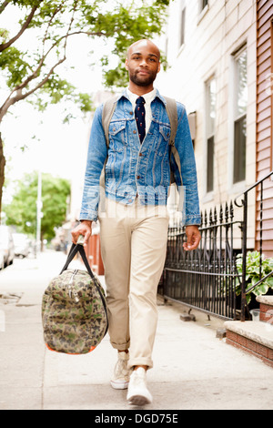 Young man walking down street with holdall Stock Photo