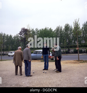 Picture from 1960s showing a group of men playing boules on a gravel courtyard next to a road, Paris, France. Stock Photo