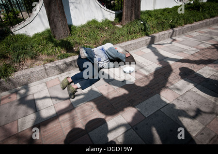 homeless man sleeping on sidewalk in Shanghai, China Stock Photo