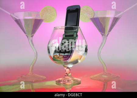 In the middle, you see a brandy glass in which a cell phone is immersed. two cocktail glasses frame the scene Stock Photo