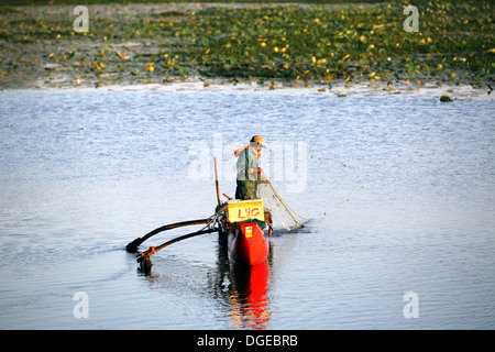 Lone Sri Lankan fisherman checking his fishing net from his simple outrigger canoe on Arugam Lagoon Stock Photo