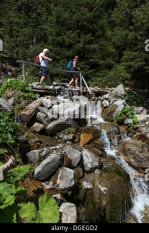Hikers crossing a wooden bridge over a waterfall. Madrisa to Klosters trail. Switzerland Stock Photo