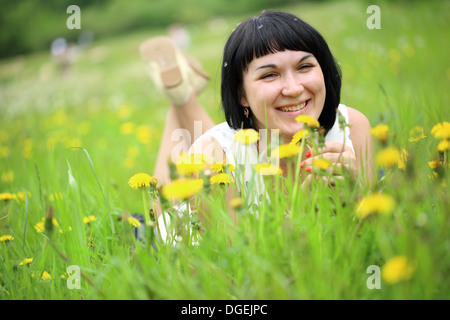 Young woman lying on grass in the field of dandelion Stock Photo