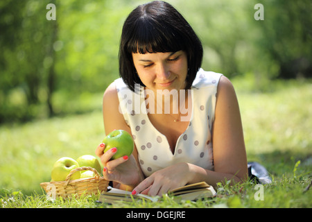 Young woman holding apple and reading book on grass Stock Photo