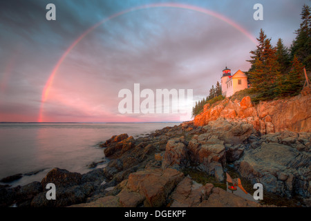 A double rainbow appears briefly at sunrise over Bass Harbor Head Lighthouse, and is reflected in a tidal pool, in Acadia National Park. Stock Photo