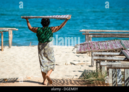 Thai woman carries a rack with squid on her head out into the sunshine for drying at the beach in Hua Hin, Thailand Stock Photo