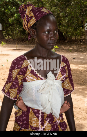 Young Gambian Woman Carrying Baby on Back. Note Feet on either side of waist. Fass Njaga Choi, North Bank Region, The Gambia. Stock Photo