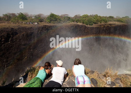 Victoria Falls Zambia, three tourists on Livingstone island, Zambia looking at the rainbow and the Victoria Falls, Africa Stock Photo