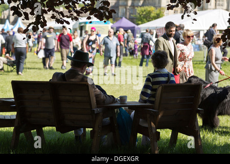 Couple taking break having drink in shade visitors walk around hot sunny Game Country Fair 2013 Burghley House Stamford England Stock Photo