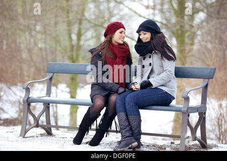 Two bestfriends sitting on a park bench and having a fun conversation Stock Photo