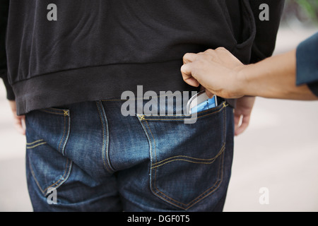 Thief stealing mobile phone from back pocket of a man walking on the street. Pickpocketing smart phone from back pocket of man. Stock Photo