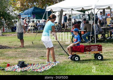 Mother pulling young son wearing blue shirt and baseball cap while seated in red Radio Flyer wagon at Cedar Key Seafood Festival Stock Photo