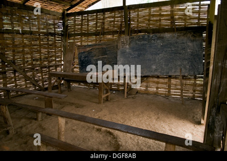 Old wooden tables in poor condition serve students & teachers in a room with a dirt floor at a primary school in communist Laos. Stock Photo