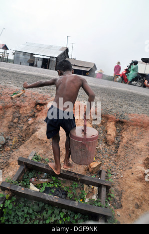 A cambodian boy carries a bucket of water from well in the rain at floating village on Tonle Sap Lake near Siem Reap, Cambodia. Stock Photo