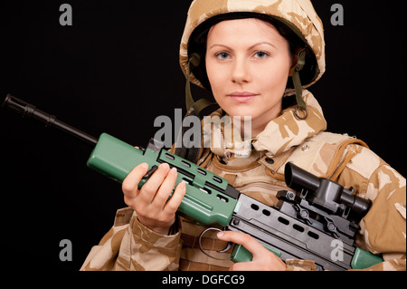 Young female soldier holding an SA80 rifle and wearing British Military desert camouflage uniform. Stock Photo