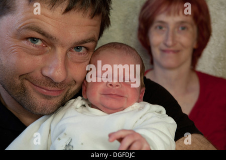 Family portrait, proud father holding his newborn boy, mother at back, Germany