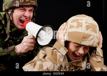 Male soldier shouting orders to a distraught female soldier with the use of a small hand held loudspeaker. British uniforms. Stock Photo