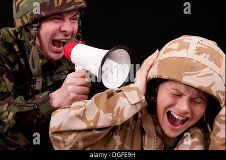 Male soldier shouting orders to a distraught female soldier with the use of a small hand held loudspeaker. British uniforms. Stock Photo