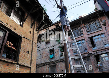 Young man standing on ladder that is leaning against power pole, Bhaktapur, Kathmandu Valley, Nepal, Asia Stock Photo