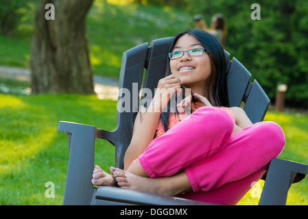 Girl sitting on garden chair looking away smiling Stock Photo