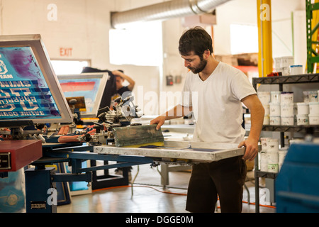 Worker pressing ink on frame in screen printing workshop Stock Photo