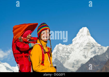 Young tourist mother carrying her little child in a rack on her back, trekking towards Ama Dablam Mountain above Namche Bazar Stock Photo