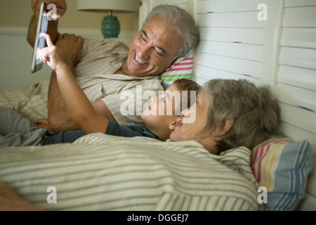 Grandparents lying down with grandson and looking at digital tablet Stock Photo