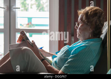 Elderly woman sitting in an armchair reading a newspaper, Grevenbroich, North Rhine-Westphalia Stock Photo