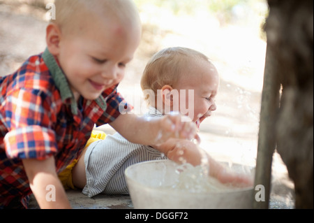 Toddler twins splashing in bowl of water Stock Photo