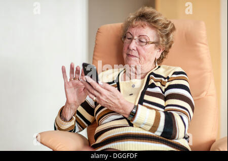 Elderly woman sitting in an armchair and using a smartphone Stock Photo