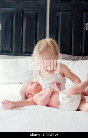Girl sitting with baby brother on bed Stock Photo