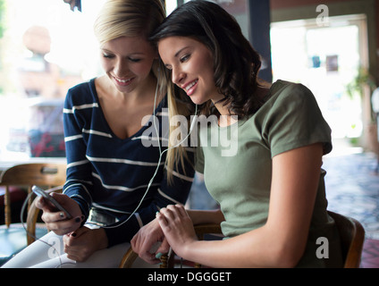 Two teenage girls sharing earphones in coffee house Stock Photo