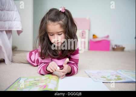 Girl lying on front and reading sticker book Stock Photo