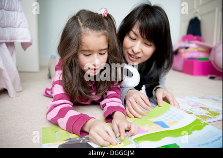 Girl lying on front and reading sticker book with mother Stock Photo