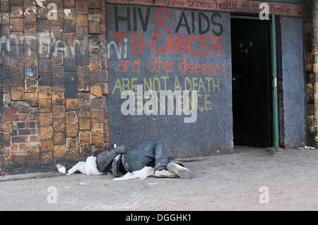 Street child sleeping in front of a doorway bearing the message, HIV & AIDS, TB cancer and other disesases are not a death Stock Photo