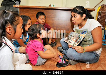 Child care worker of the Mexican non-governmental organization CIDES reading a picture book to indigenous children in a slum Stock Photo