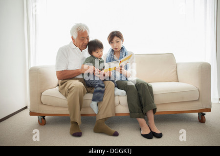 Mother reading to son sitting on grandfather's lap Stock Photo