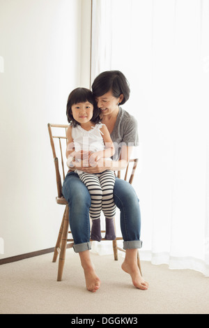 Mother and daughter sitting on wooden chair, portrait Stock Photo