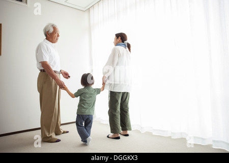 Three generation family standing by window holding hands Stock Photo