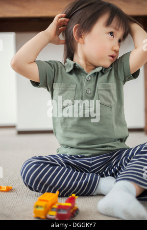Boy sitting on floor with hands in hair Stock Photo