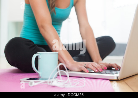 Young woman on yoga mat using laptop Stock Photo