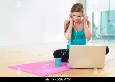 Young woman on yoga mat listening to smartphone Stock Photo