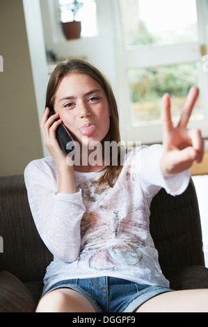 Teenage girl on phone making peace sign with tongue out Stock Photo