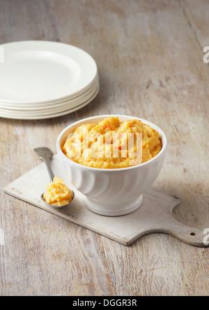 Carrot, swede and potato mash in rustic white bowl with large metal spoon Stock Photo