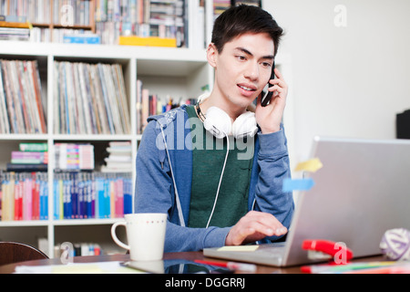 Male student on cell phone using laptop Stock Photo