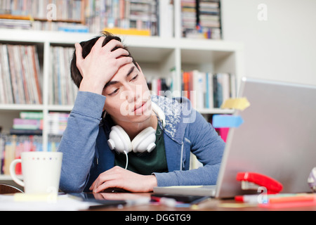 Worried male student with hand in hair using laptop Stock Photo